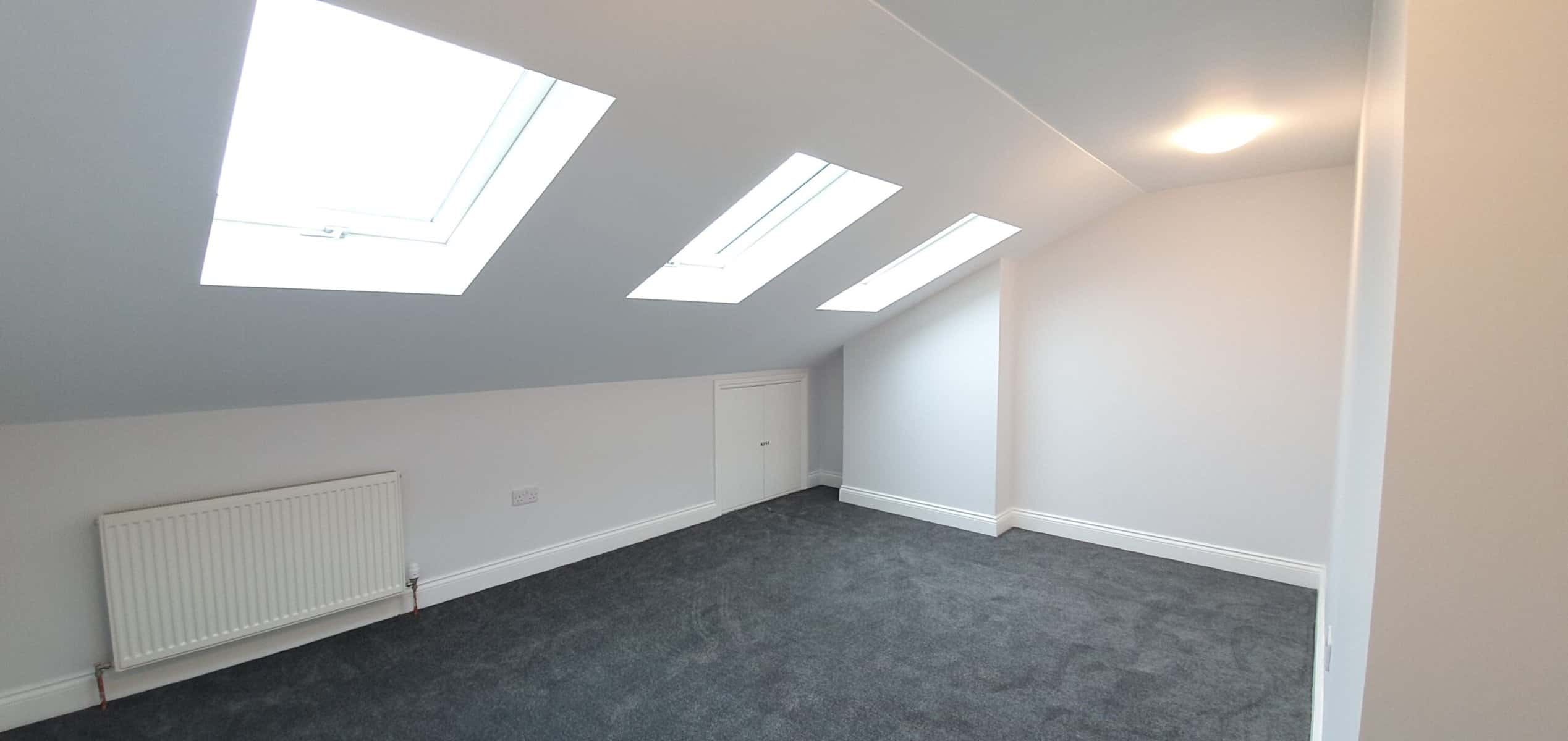 Modern loft conversion with skylights, white walls, grey carpet, and built-in storage, creating a bright and functional attic space in London