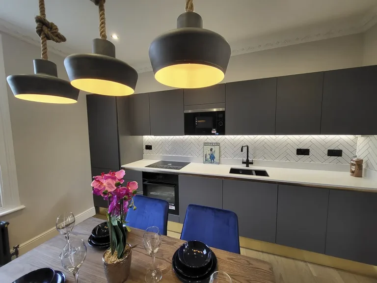 Modern kitchen renovation with sleek dark cabinetry, gold accents, and industrial pendant lighting.