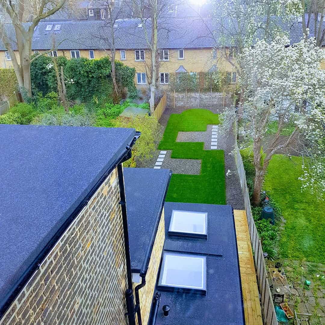 Builders in Hanwell and Greenford A modern double-storey extension with a side return, featuring a black flat roof with skylights, overlooking a landscaped garden with geometric lawn design.